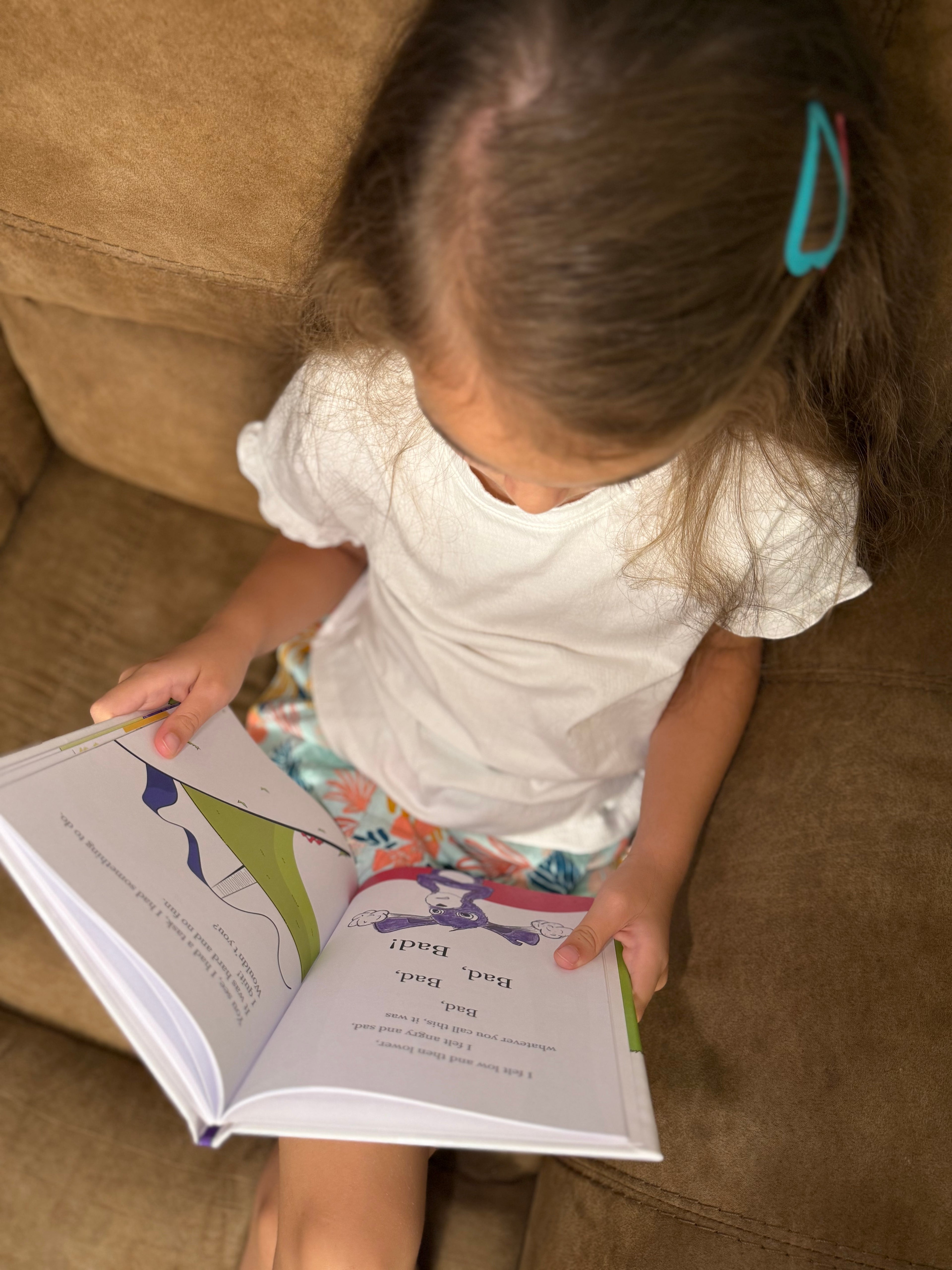 Little girl sitting on a couch reading her book.