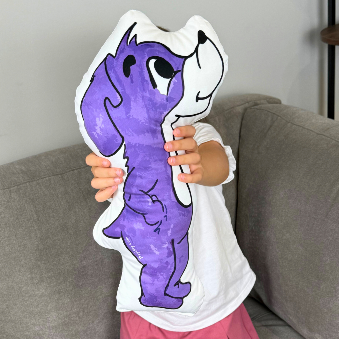 Child holding a large purple and white cartoon dog pillow against a gray couch.