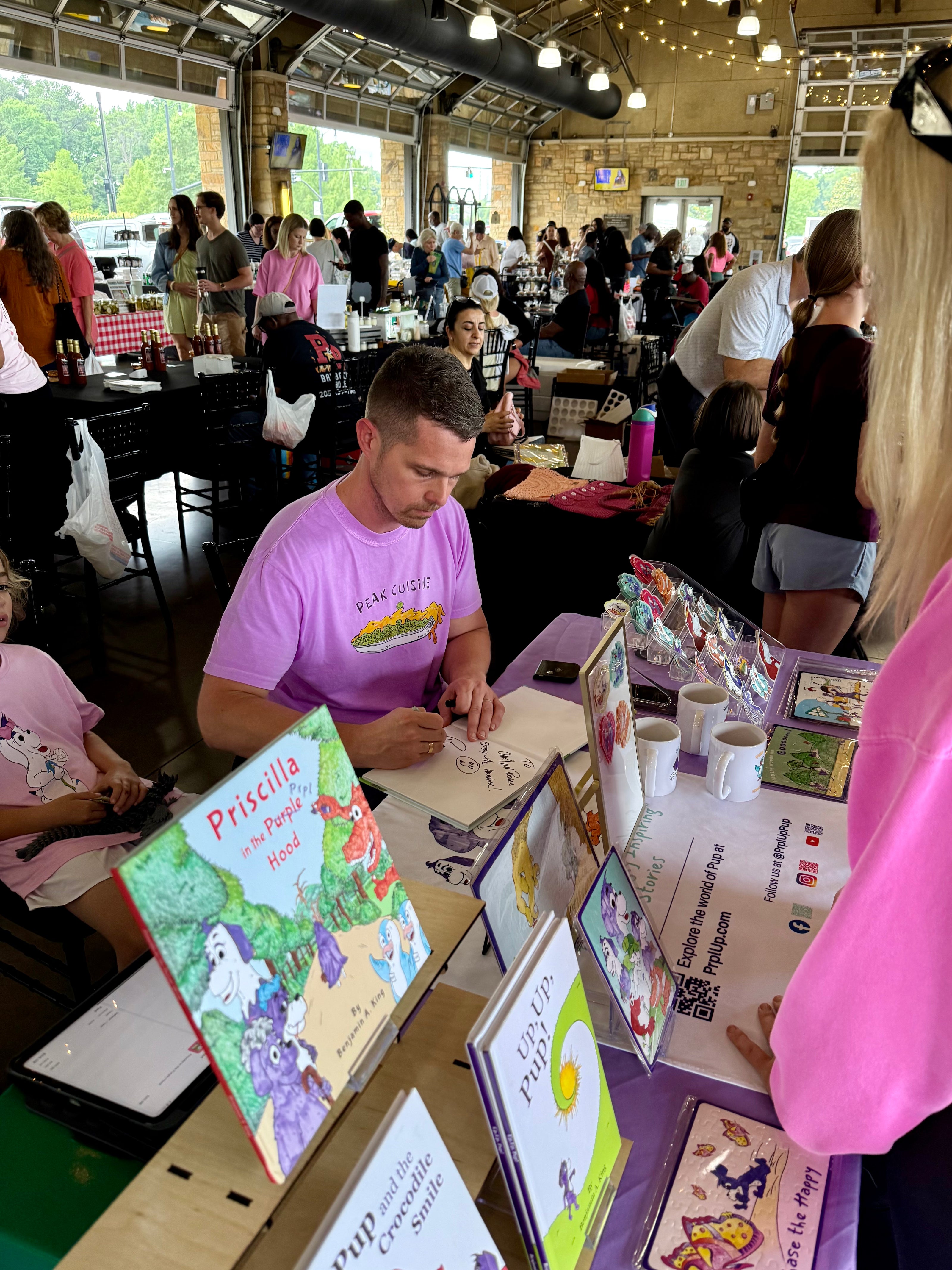Benjamin A. King signing books at the Tuscaloosa River Market event with people in the background.