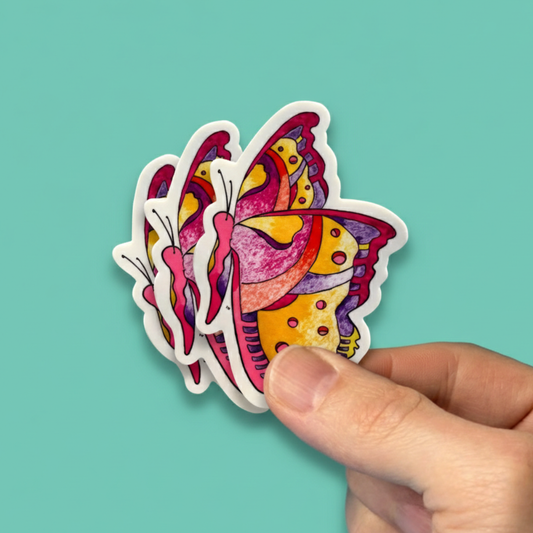Colorful butterfly-shaped sticker held by a hand against a teal background. Inspired by the Prpl Up Pup world.