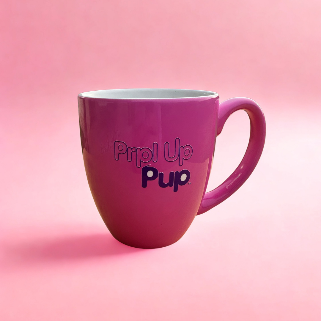 A pink ceramic coffee mug with the text 'Prpl Up Pup' printed on the back, set against a solid pink background.