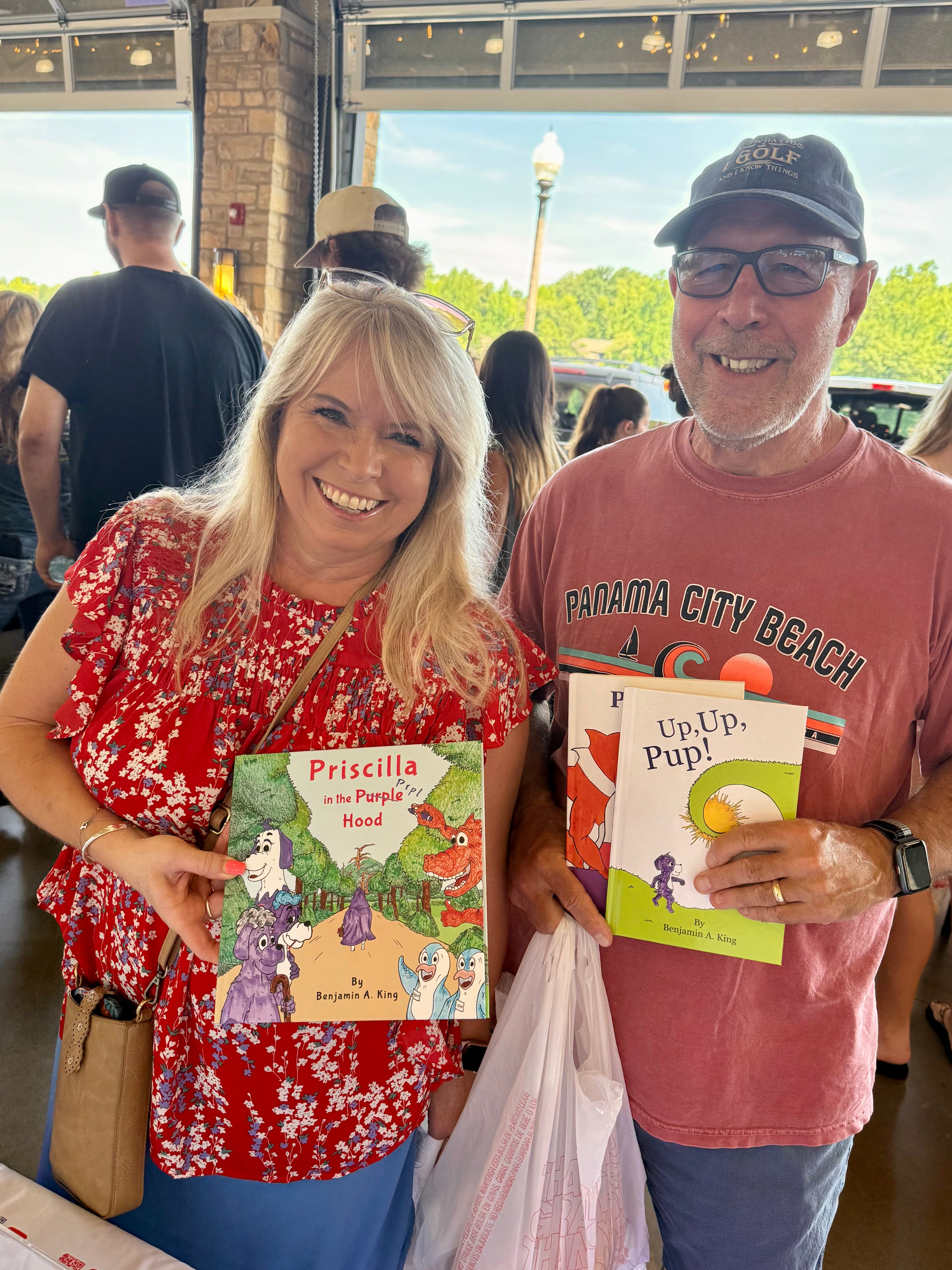 Two grandparents holding Prpl Up Pup picture books for kids at the Tuscaloosa River Market. 