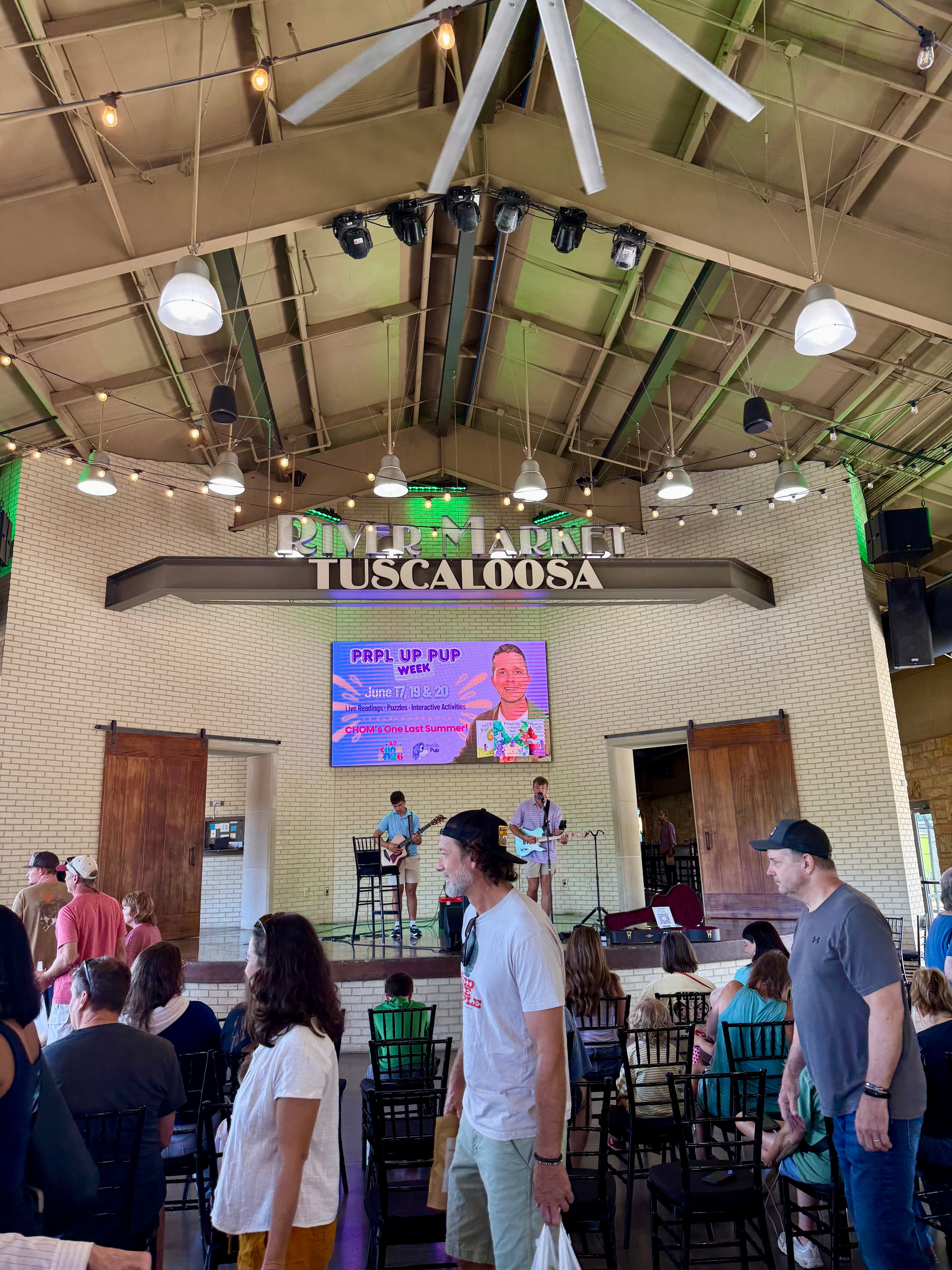 Tuscaloosa River Market is a large indoor venue with a stage and audience. Monitor features the Prpl Up Pup Week with author and illustrator, Benjamin A. King.