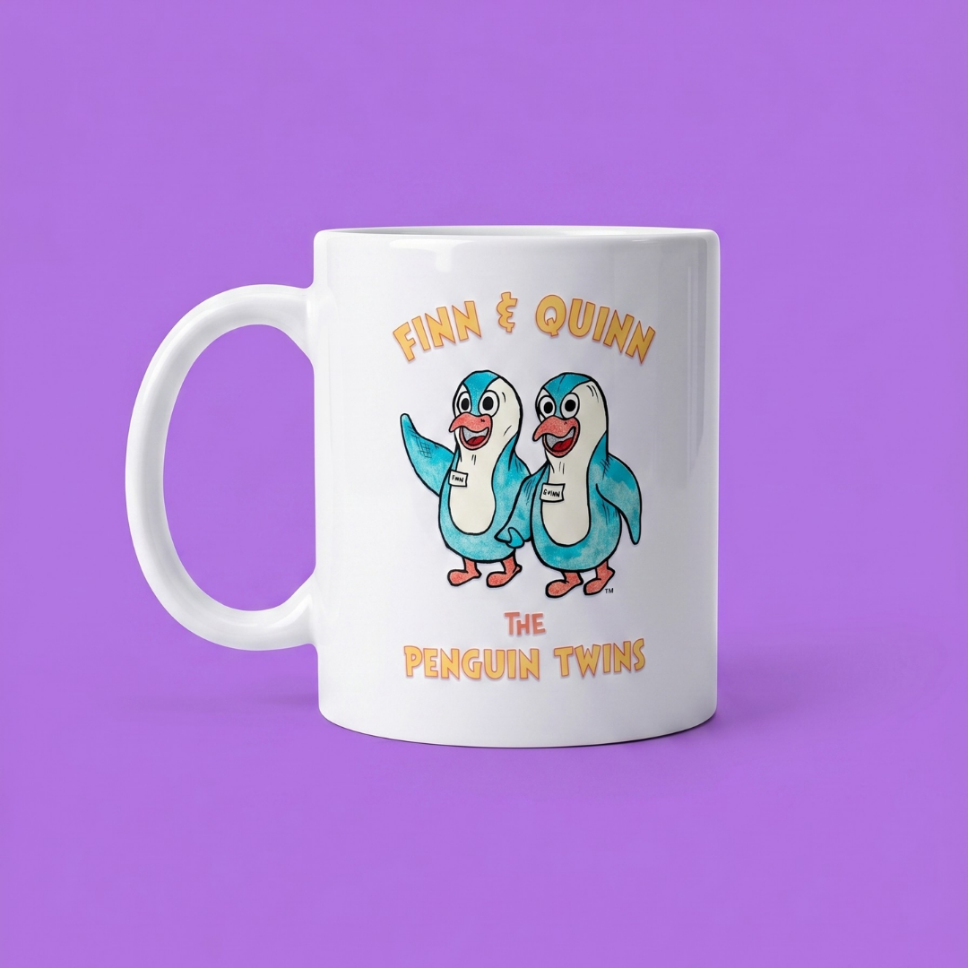 A white ceramic mug featuring a cartoon illustration of two penguin twins with the text 'FINN & QUINN THE PENGUIN TWINS' in orange, set against a solid purple background.