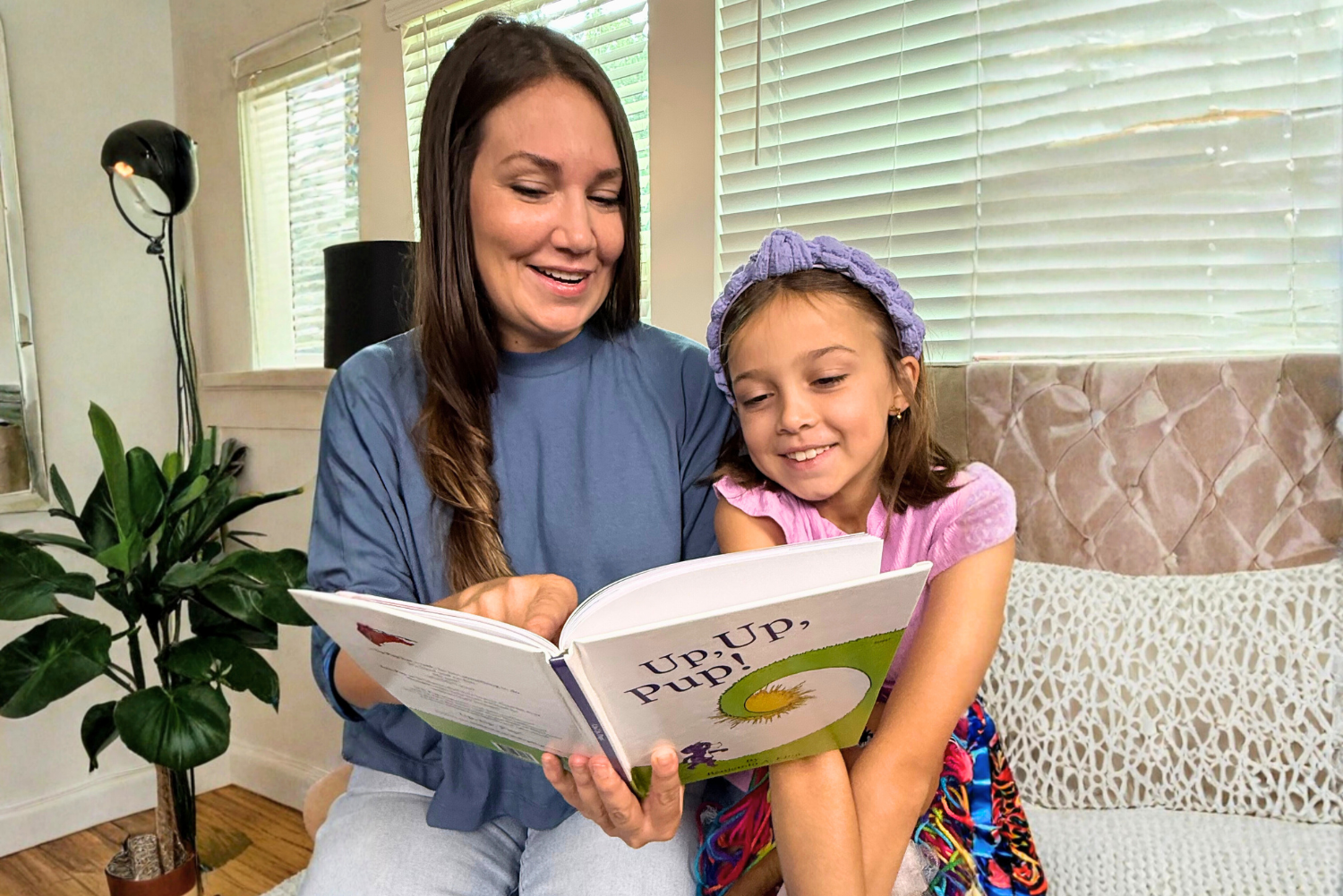 Woman and child reading a book together on a couch in a home setting