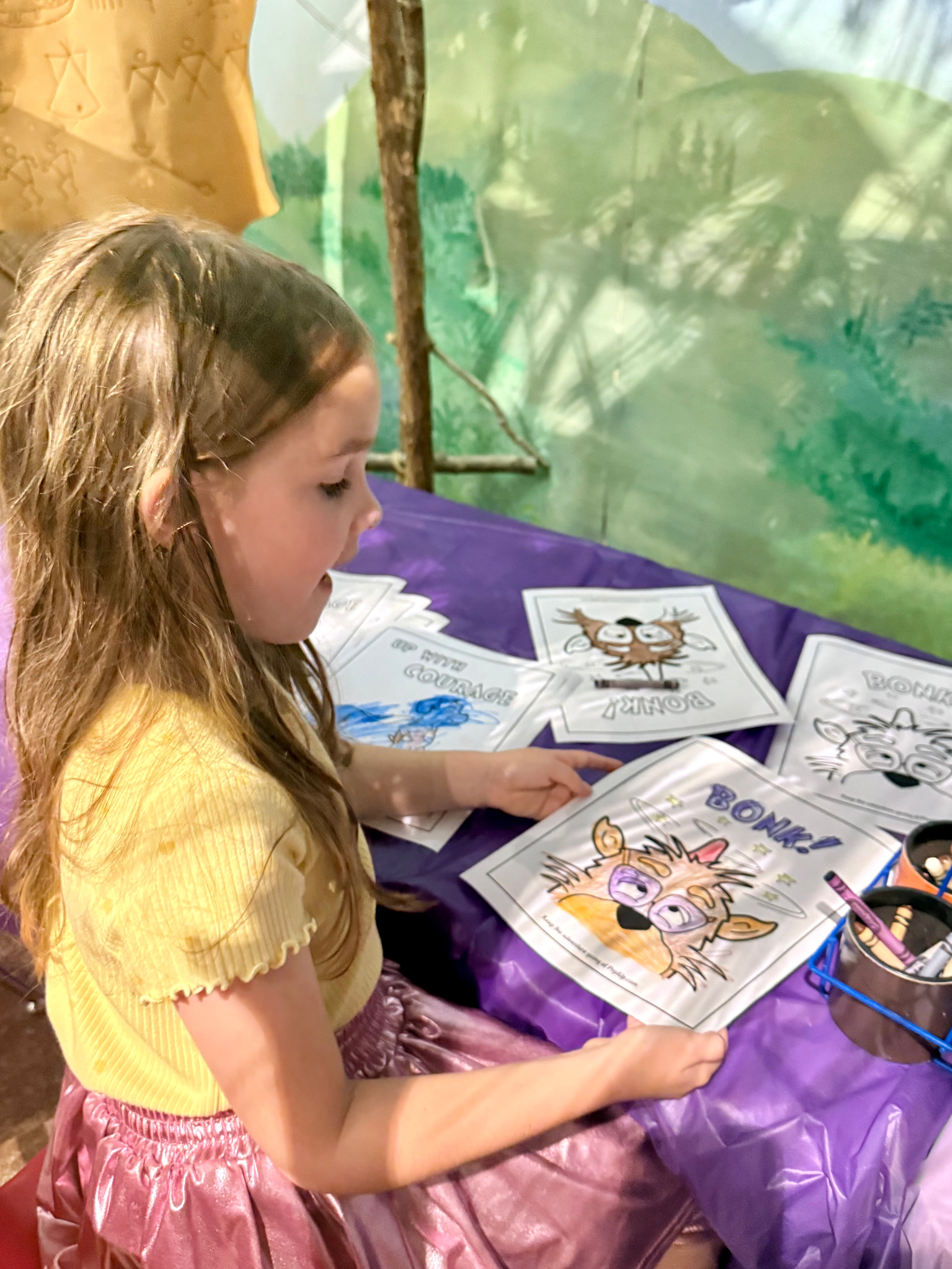 Young girl coloring characters from the World of Prpl Up Pup at a table, with coloring sheets and crayons.