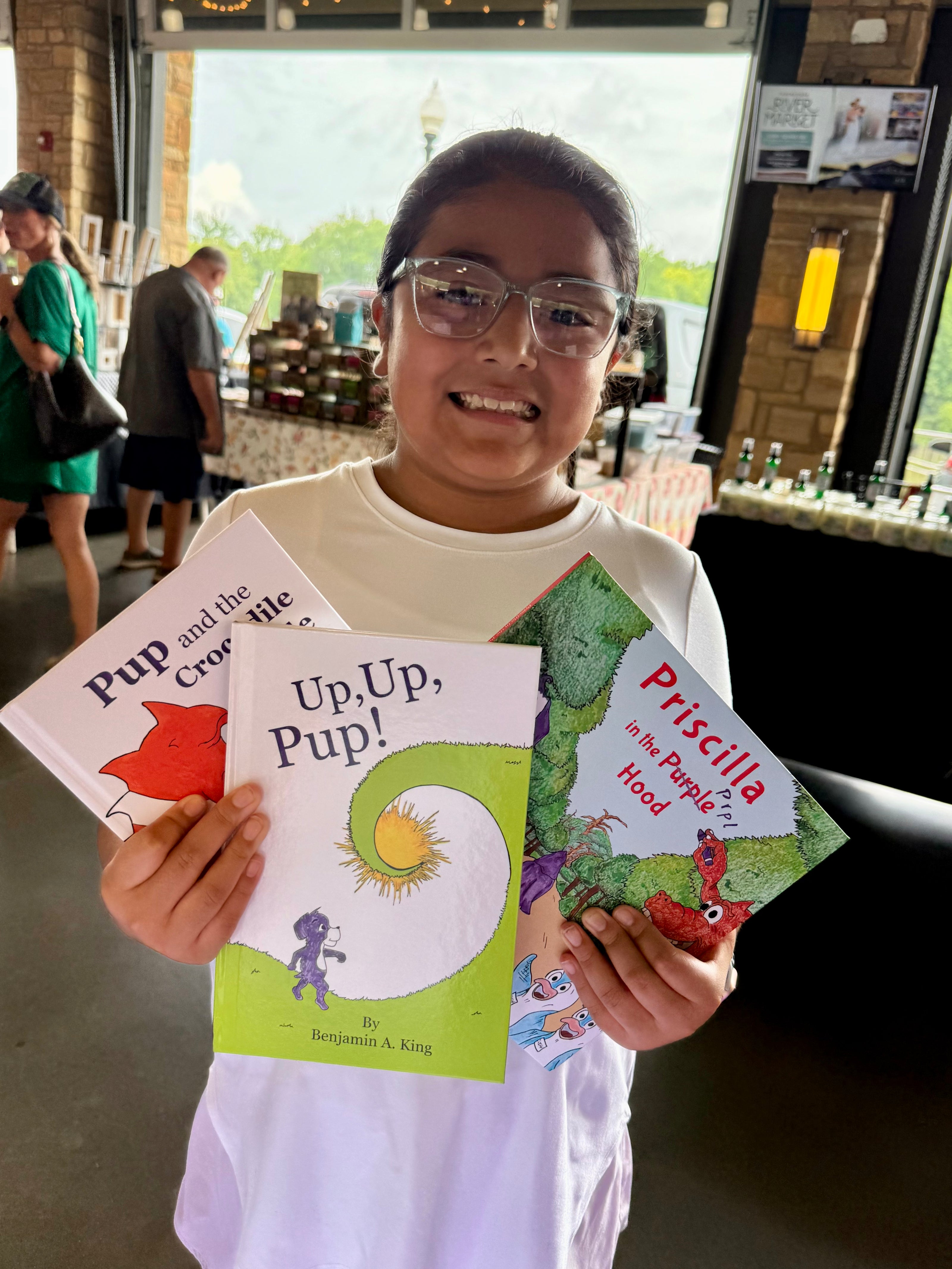 Young girl holding her three children's books, Prpl Up Pup's story books collection, at the Tuscaloosa River Market in Alabama.
