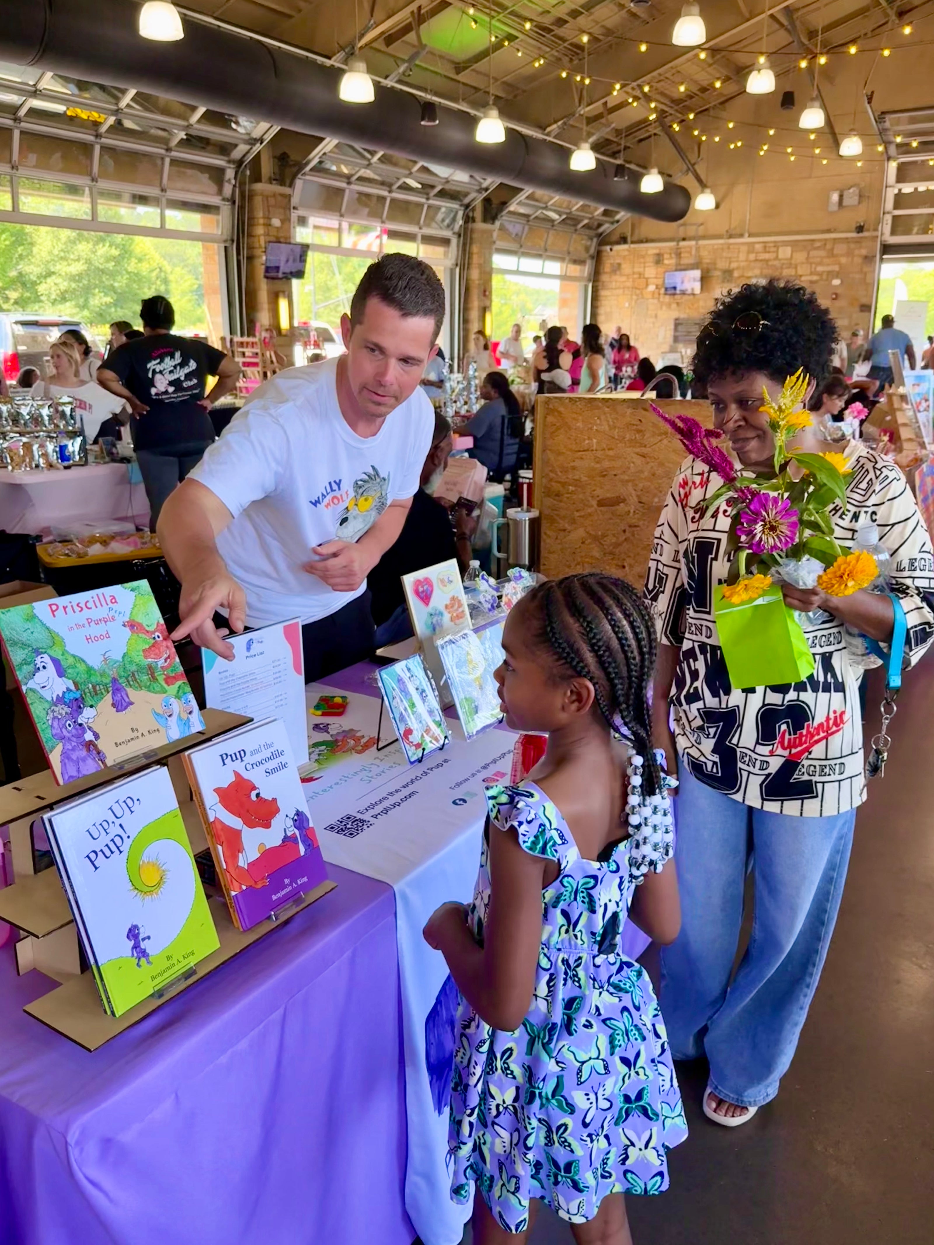 Benjamin A. King showing his picture books to a mom and her young girl at the Tuscaloosa River Market. 